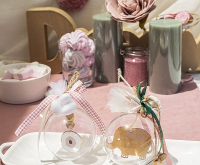 Μπομπονιέρες με διάφανο κουτί σε σχήμα μπάλας διακοσμημένες με ξύλινο στοιχείο ελεφαντάκι, μεταλλικό στοιχείο μάτι και διάφορες κορδέλες