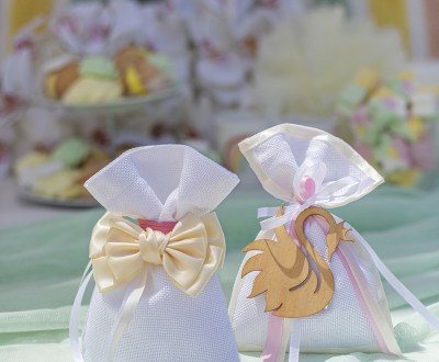 Μπομπονιέρες με λευκό πουγκί διακοσμημένες με υφασμάτινο φιόγκο, ξύλινο στοιχείο κύκνο και διάφορες κορδέλες