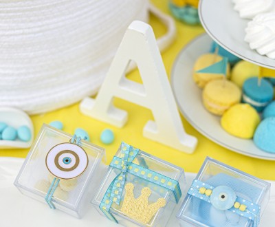 Μπομπονιέρες με διάφανα plexi κουτάκια διακοσμημένες με μεταλλικό και κεραμικό στοιχείο μάτι, υφασμάτινη κορώνα και διάφορες κορδέλες