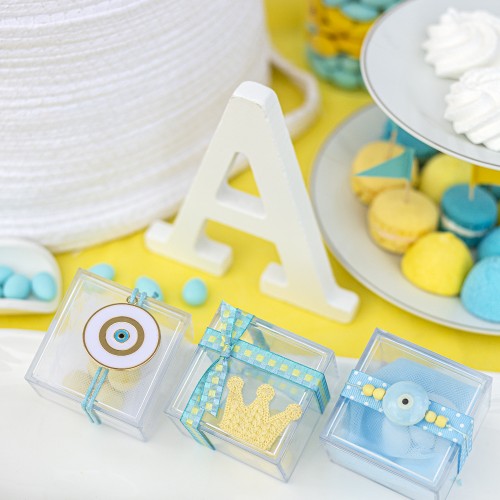 Μπομπονιέρες με διάφανα plexi κουτάκια διακοσμημένες με μεταλλικό και κεραμικό στοιχείο μάτι, υφασμάτινη κορώνα και διάφορες κορδέλες