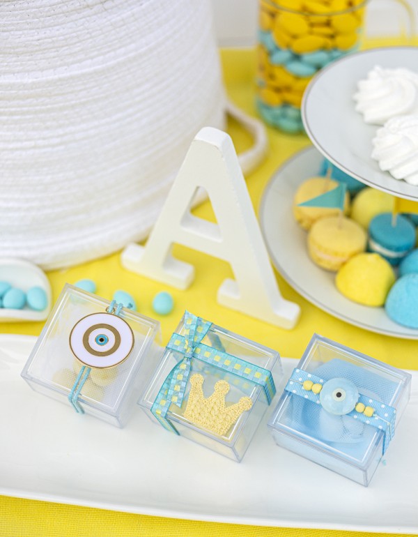 Μπομπονιέρες με διάφανα plexi κουτάκια διακοσμημένες με μεταλλικό και κεραμικό στοιχείο μάτι, υφασμάτινη κορώνα και διάφορες κορδέλες