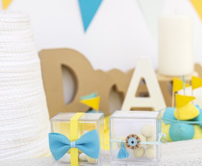 Μπομπονιέρες με διάφανα plexi κουτάκια διακοσμημένες με υφασμάτινο φιόγκο, ξύλινο στοιχείο μάτι και σατέν κορδέλα