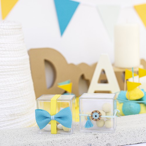 Μπομπονιέρες με διάφανα plexi κουτάκια διακοσμημένες με υφασμάτινο φιόγκο, ξύλινο στοιχείο μάτι και σατέν κορδέλα