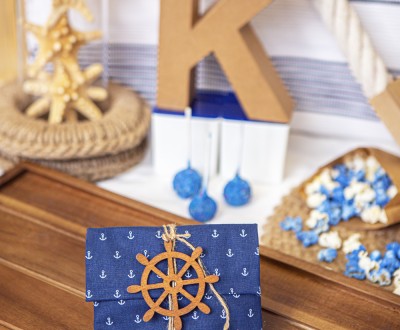 Μπομπονιέρα σε σχήμα φάκελο με ύφασμα με pattern άγκυρες διακοσμημένη με ξύλινο στοιχείο πηδάλιο και τσουβαλέ κορδόνι