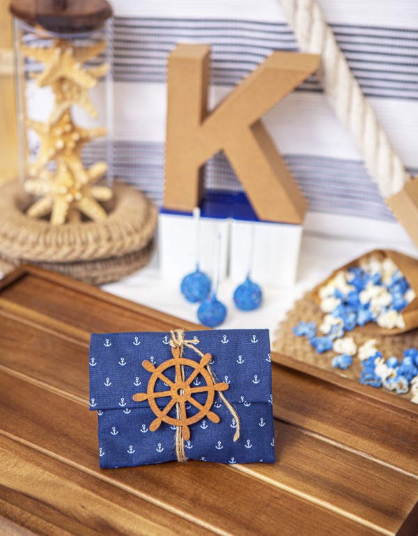 Μπομπονιέρα σε σχήμα φάκελο με ύφασμα με pattern άγκυρες διακοσμημένη με ξύλινο στοιχείο πηδάλιο και τσουβαλέ κορδόνι