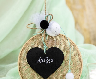 Μπομπονιέρα με ξύλινο στεφάνι και ύφασμα τσουβαλέ διακοσμημένη με ξύλινο στοιχείο πίνακα σε σχήμα καρδιάς και διάφορες μπάλες πομ πομ