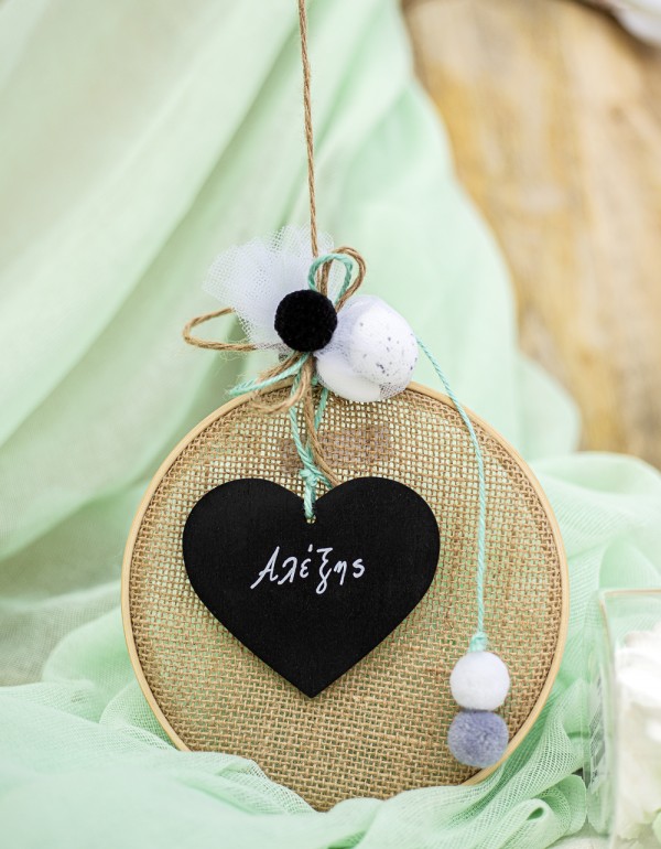 Μπομπονιέρα με ξύλινο στεφάνι και ύφασμα τσουβαλέ διακοσμημένη με ξύλινο στοιχείο πίνακα σε σχήμα καρδιάς και διάφορες μπάλες πομ πομ